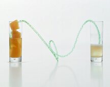 A long drinking straw connecting a glass of sparkling wine to a glass of fruit-juice ice cubes