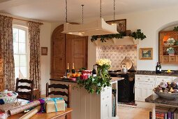 Open-plan, country-house kitchen with free-standing counter below suspended, overhead lighting unit; dining area with wrapped presents in foreground