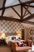 Récamier at foot of double bed against wall with floral wallpaper in rustic attic bedroom
