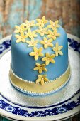 A layer cake iced with blue fondant, decorated with marzipan flowers and sugar balls