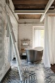 Ladder used as towel rack, vintage bathtub behind curtain in corner of room with whitewashed brick walls and patterned tiled floor