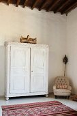 White wooden cupboard in spacious room with high ceiling, armchair and Moroccan rug