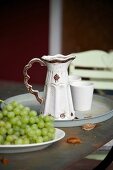 Vintage ceramic jug and beaker on metal tray next to plate of grapes