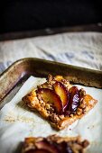 Puff pastry square with red plum crumble on a baking sheet; close-up