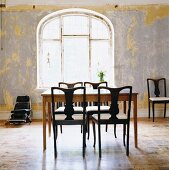 Schlichter Tisch und elegante dunkle Holzstühle vor Fenster mit Rundbogen in renovierbedürftigem Esszimmer