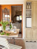 Small fridge concealed in wooden cupboard and set table on veranda with country-style furnishings