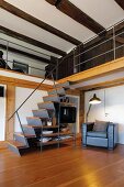 Metal staircase with wooden treads and integrated shelving next to standard lamp and armchair below gallery in rustic interior