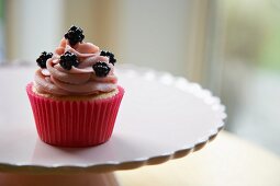 Cupcake topped with blackberries, on a cake stand