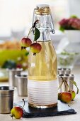 Apple liqueur in a decorative flip top bottle with ornamental apples and small pewter mugs next to it