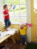 Two toddlers playing with fly swats on veranda
