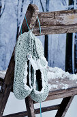 Crocheted slippers hanging on rustic chair in artificial winter atmosphere