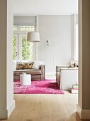 White arc lamp above grey living room sofa in pale interior with pink rug