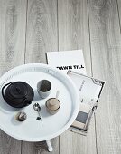 Cast iron teapot, teacup and sugar bowl on white tray table on wooden floor