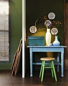 Pastel blue table and stool against olive green wall; collection of china plates on wall