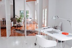 Weisser Arbeitsplatz im Designerstil mit Retroflair auf weiss lackiertem Dielenboden vor offenen Drehtüren und Blick ins Wohnzimmer auf Holzboden mit Zebrafell