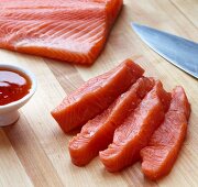 Pieces of Freshly Cut Salmon Steak on a Wooden Board with a Little Bowl of Chili Sauce