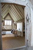 Comfortable double bed on floor below steep, exposed roof structure of half-timbered house