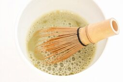 Matcha tea in a bowl with a tea whisk (close-up)