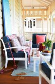 White wooden bench and armchairs with dark blue cushions around table on veranda with white balustrade and turned columns