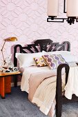 Double bed with black frame against pink wallpaper with graphic pattern