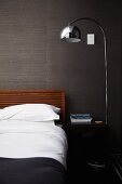 Purist double bed, shiny standard lamp and black bedside table against grey, structured wallpaper