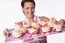 A woman holding a tray of cupcakes topped with letters reading 'Merry Xmas'