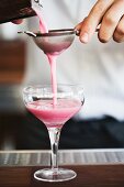 Straining a Pink Cocktail into a Glass