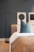 Schlicht gehaltenes Schlafzimmer mit dunklen Wänden, Bett, Stehlampe & Wandbildern