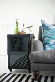 Side table with glass door on castors next to grey armchair