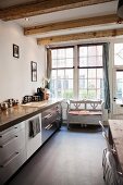 Kitchen counter with stainless steel fronts and rustic bench below lattice window