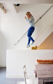 Young woman on staircase behind partially visible wooden table and chair and half-height wall