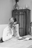 Young woman reading magazine at table (B&W photo)