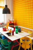 Bunt lackierte Stühle und weiße Sitzbank um Esstisch vor Wand mit gelber Punkte-Tapete