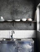 Purist, industrial-style kitchen with stainless steel base unit and sink below simple shelf on grey wall