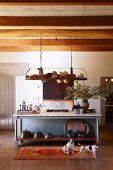 Long foyer with wood-beamed ceiling and collection of hats on shelf suspended above wooden table; contented dogs on rug