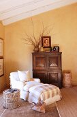 Armchair and matching footstool next to rattan side table and wooden cupboard against yellow-painted wall in attic interior