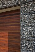 Gabion house facade and door of mahogany-coloured wooden slats