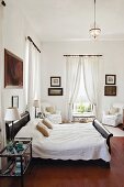 Schlafzimmer mit drapierten, weissen Vorhängen, Kunstsammlung an den Wänden und Doppelbett im Kolonialstil