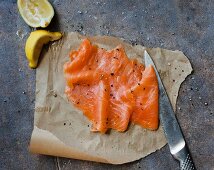 Smoked salmon, a knife and lemon wedges on grease-proof paper