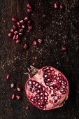 Half a pomegranate and pomegranate seeds on a wooden surface