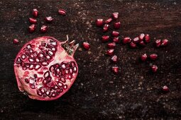 Half a pomegranate and pomegranate seeds on a wooden surface