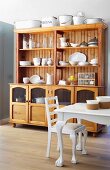 Pale wooden dresser in dining room with white-painted dining table and white chair; collection of vintage enamel vessels on dresser