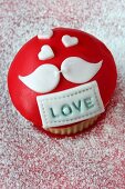 A cupcake iced with the word LOVE and a pair of lovebirds, for Valentine's Day