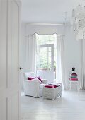 Ganzes Schlafzimmer in Weiß - weißer Hussensessel mit weiß gestrichener Korbtruhe auf weißem Dielenboden vor weißen bodenlangen Vorhängen