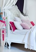 Romantic, white canopied bed with many scatter cushions in various pastel shades