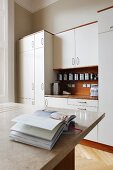 Open cookery book on counter with marble worksurface in front of fitted cupboards with white doors and wooden worksurface