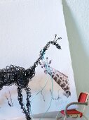 Giraffenfigur aus schwarzem Draht vor Giraffenmotiv und weißem Hintergrund