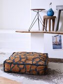 Floor cushion with animal-skin pattern on animal-skin rug and various stools on rustic, wooden surface