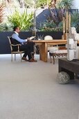 Man sitting at rustic wooden table, plants in terraced beds and stone crosses on rustic wooden bench in foreground