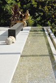 Long, narrow pool adjoining terrace, black bench, stone spheres and sculpture in background